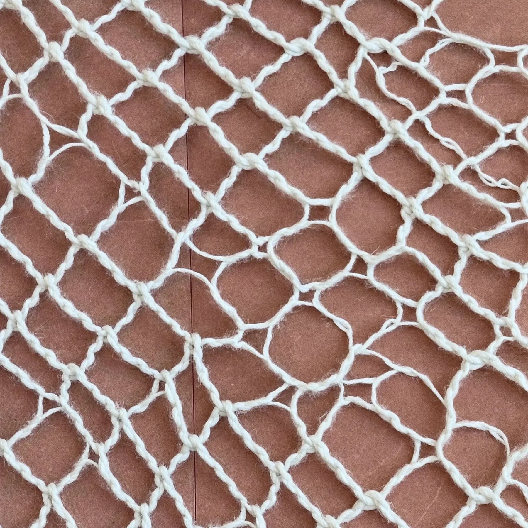 Close-up of a knotted cotton net against a rose background